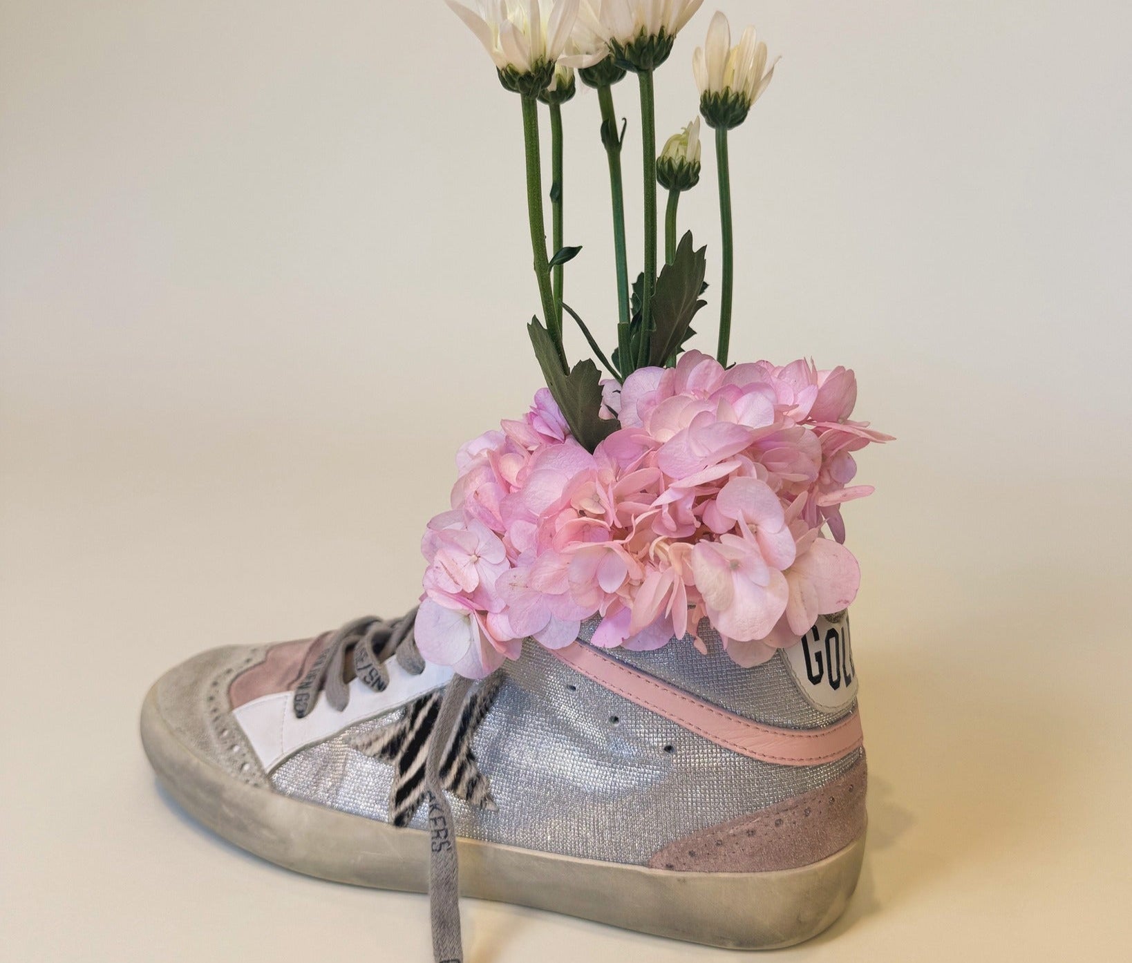 Silver high-top sneaker with pink accents holding flowers on a beige background